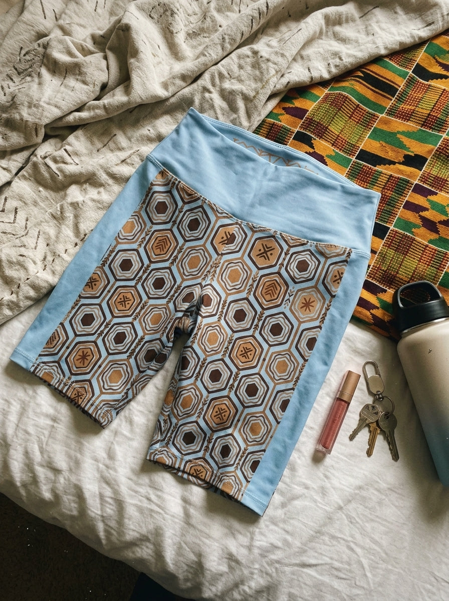 AnanseNova™ Biker Shorts in Igwe Blue, flat lay on bed with accessories — SunBorn