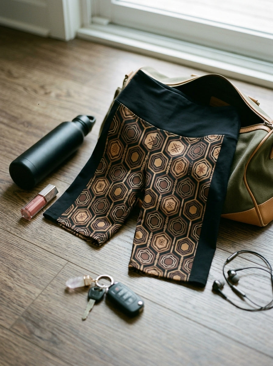 AnanseNova™ Biker Shorts in Oji Black, flat lay on wood floor with gym bag, water bottle and keys — SunBorn