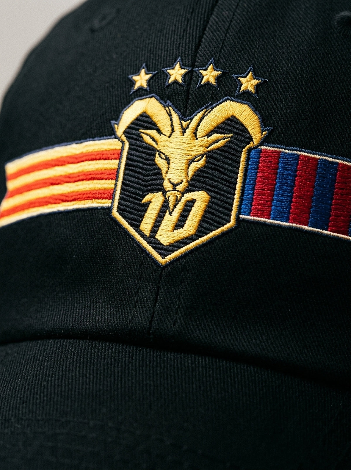 Close-up of the unlimited-colour embroidery on the GOAT Catalan dad hat in Oji Black — gold goat, No. 10 and the split Senyera and blaugrana banner in full-tone thread.