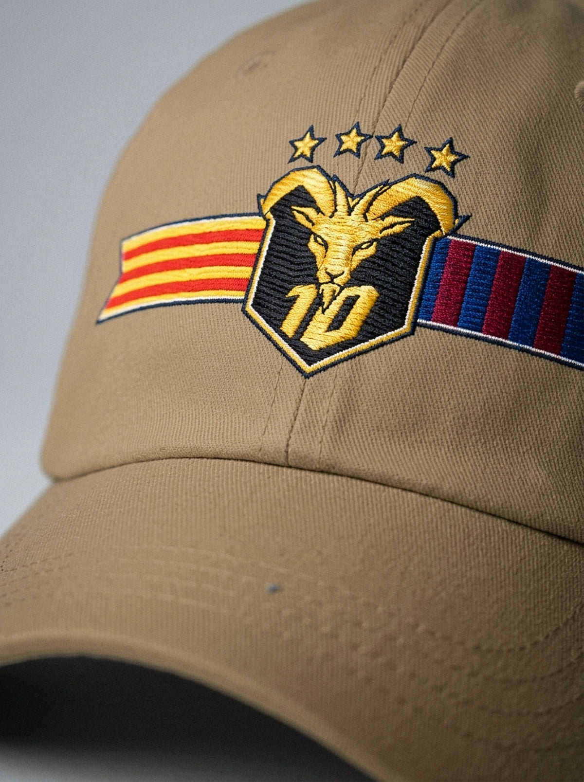 Close-up of the unlimited-colour embroidery on the GOAT Catalan dad hat in Aja Sand — gold goat, No. 10 and the split Senyera and blaugrana banner in full-tone thread.