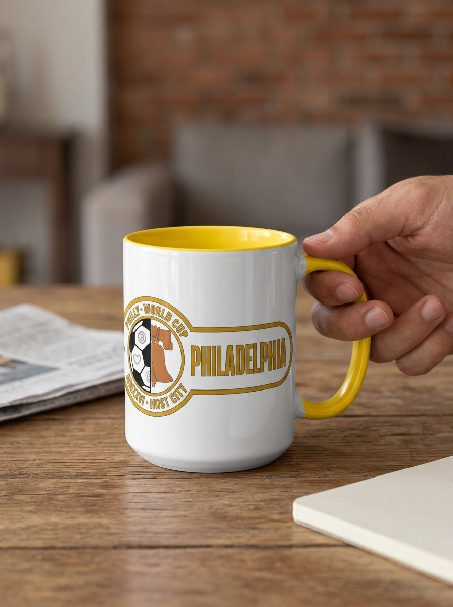 Liberty Protocol Philly '26 Mug — White Ceramic with Yellow interior, held by the handle in a living room with exposed brick
