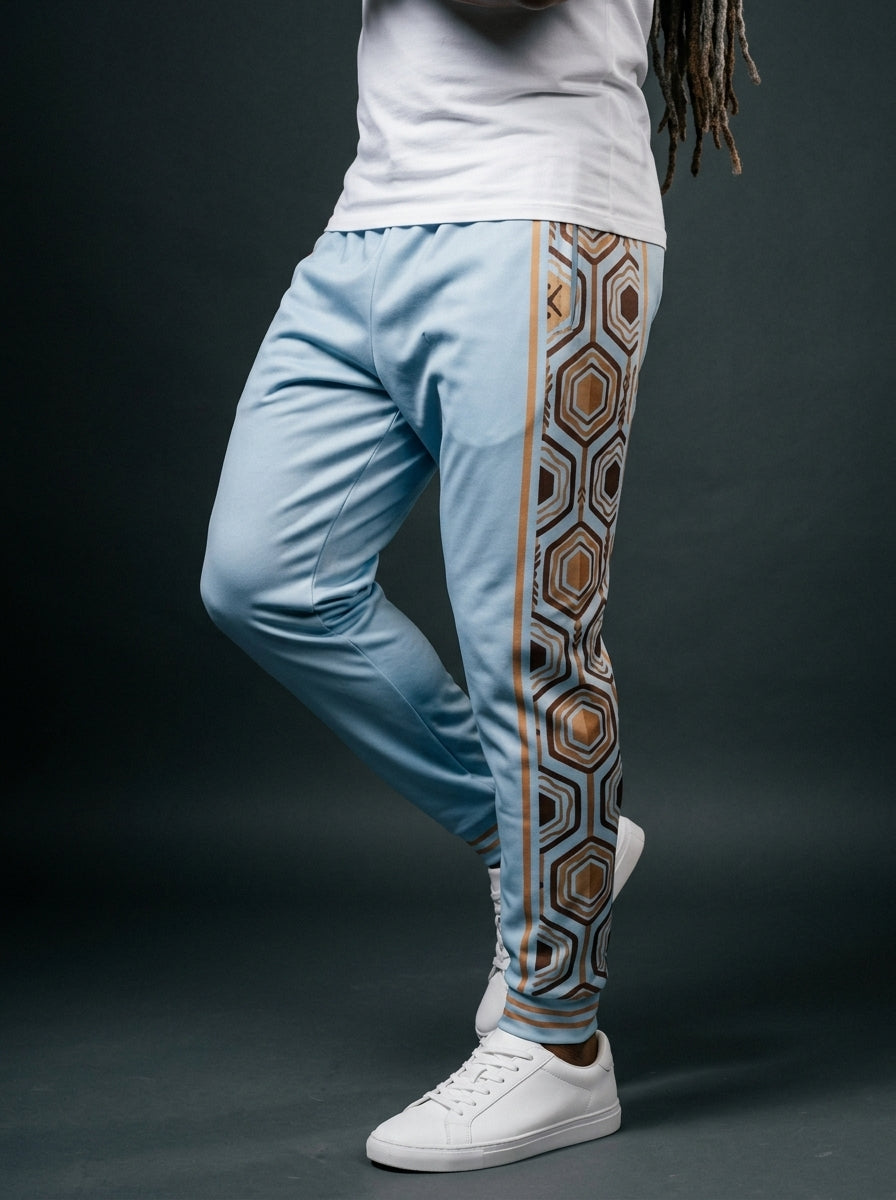 AnanseNova™ Men's Joggers in Igwe Blue, three-quarter left view on model — hexagon web-cell side panel with bronze pinstripe. SunBorn