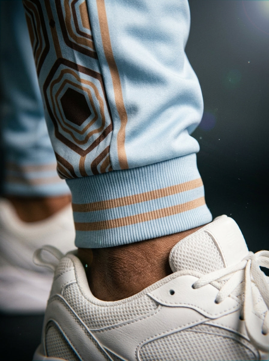 AnanseNova™ Men's Joggers in Igwe Blue, close-up of the bronze-striped ribbed ankle cuff and hexagon panel detail. SunBorn