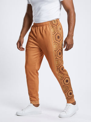 AnanseNova™ Men's Joggers in Sango Orange, three-quarter left view on model — hexagon web-cell side panel with bronze pinstripe. SunBorn