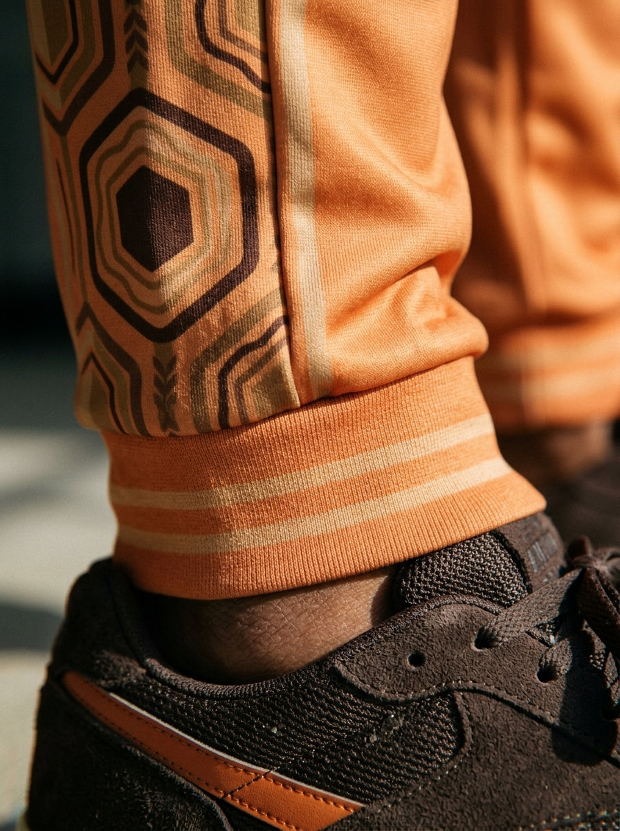 AnanseNova™ Men's Joggers in Sango Orange, close-up of the bronze-striped ribbed ankle cuff and hexagon panel detail. SunBorn