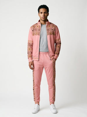 AnanseNova™ Track Jacket + Joggers Set in Eze Pink, front view on model: pink track jacket with brown and gold hexagon print yoke and sleeves, gold sleeve stripes, matching joggers with hex side stripes