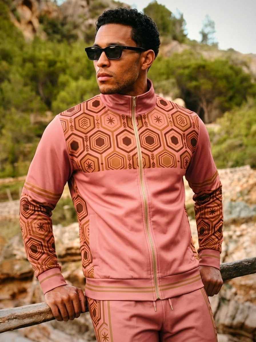 AnanseNova™ Track Jacket + Joggers Set in Eze Pink, lifestyle shot: model in sunglasses leaning on a wooden rail above a rocky Mediterranean hillside
