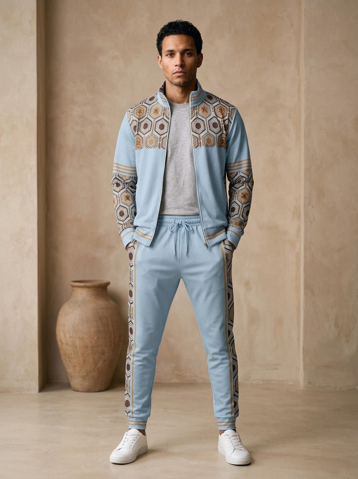 AnanseNova™ Track Jacket + Joggers Set in Igwe Blue, front view on model: light blue track jacket with brown and gold hexagon print yoke and sleeves, gold sleeve stripes, matching joggers with hex side stripes