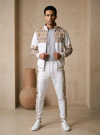 AnanseNova™ Track Jacket + Joggers Set in Ocha White, front view on model: white track jacket with brown and gold hexagon print yoke and sleeves, gold sleeve stripes, matching white joggers with hex side stripes