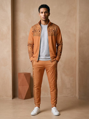 AnanseNova™ Track Jacket + Joggers Set in Sango Orange, front view on model: orange track jacket with brown and gold hexagon print yoke and sleeves, gold sleeve stripes, matching orange joggers with hex side stripes