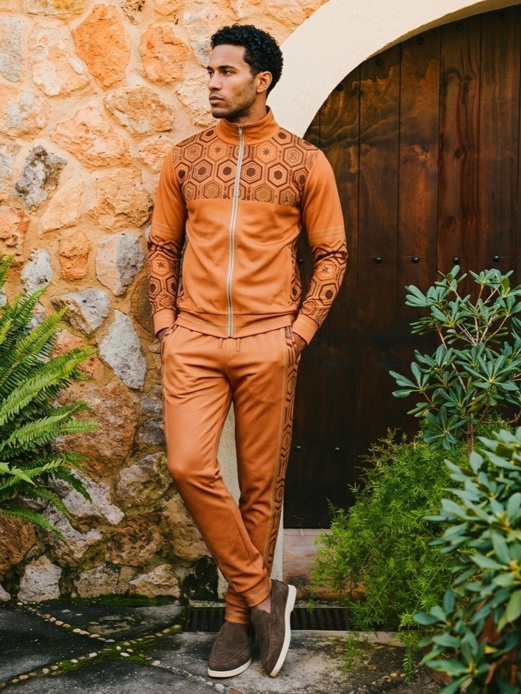 Man leaning against a stone wall beside a wooden arched door, wearing the AnanseNova™ Track Jacket + Joggers Set in Sango Orange