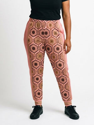 AnanseNova™ Women's Joggers in Adaeze Pink, front view on model, full-front bronze and brown hexagon print with pink side panels, bronze side stripes and striped cuffs | SunBorn