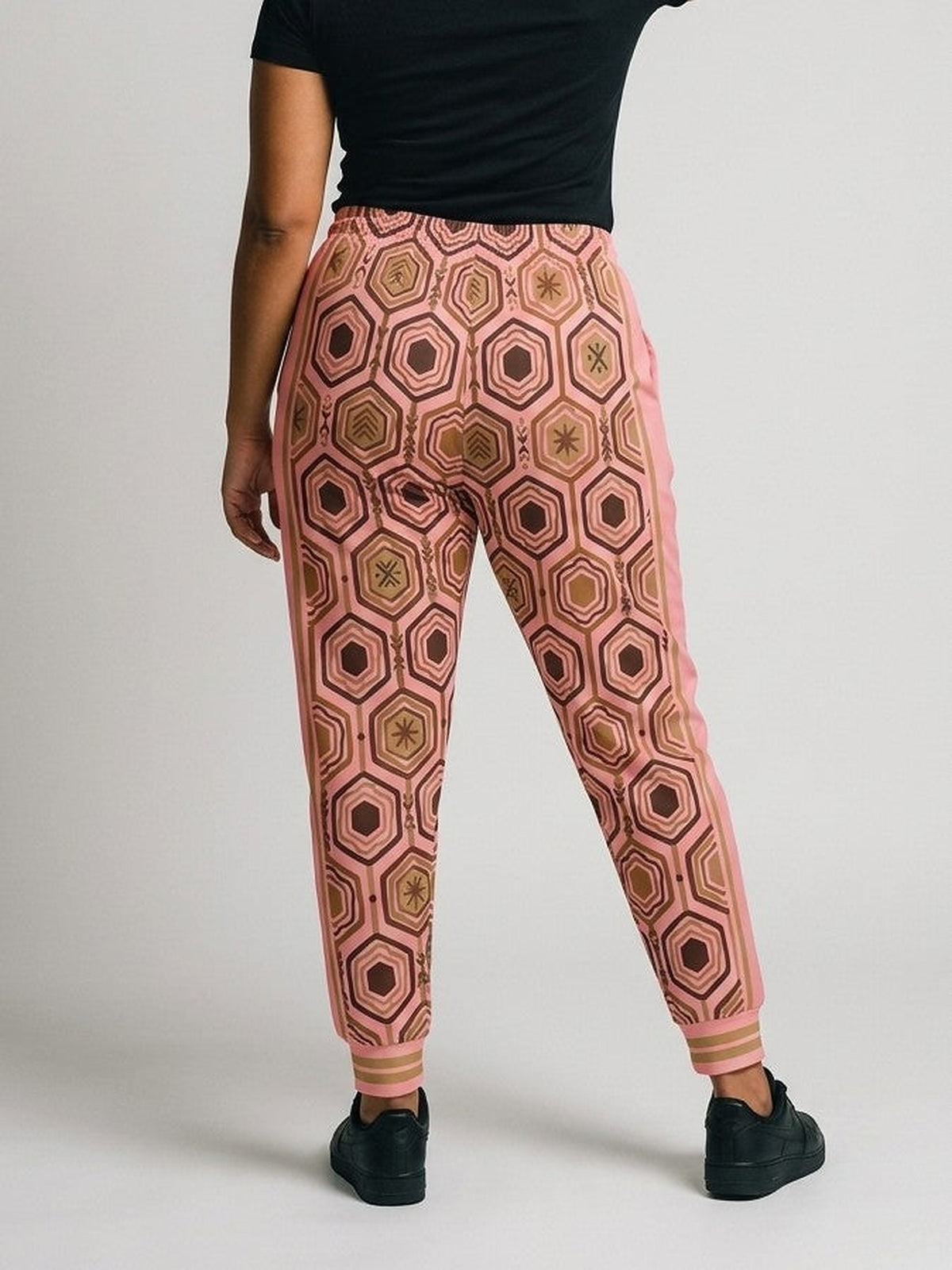 Back view of AnanseNova™ Women's Joggers in Adaeze Pink on model, hexagon print continuing across the seat and legs, styled with a black tee