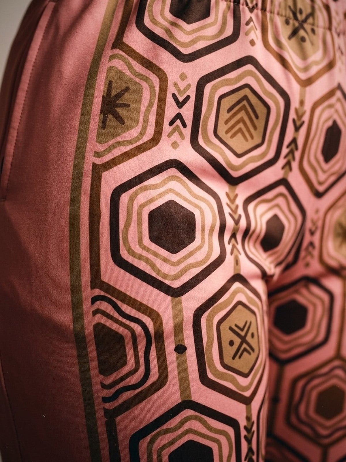 Close-up of the sublimation-printed AnanseNova™ hexagon pattern and bronze side stripe on Adaeze Pink women's joggers