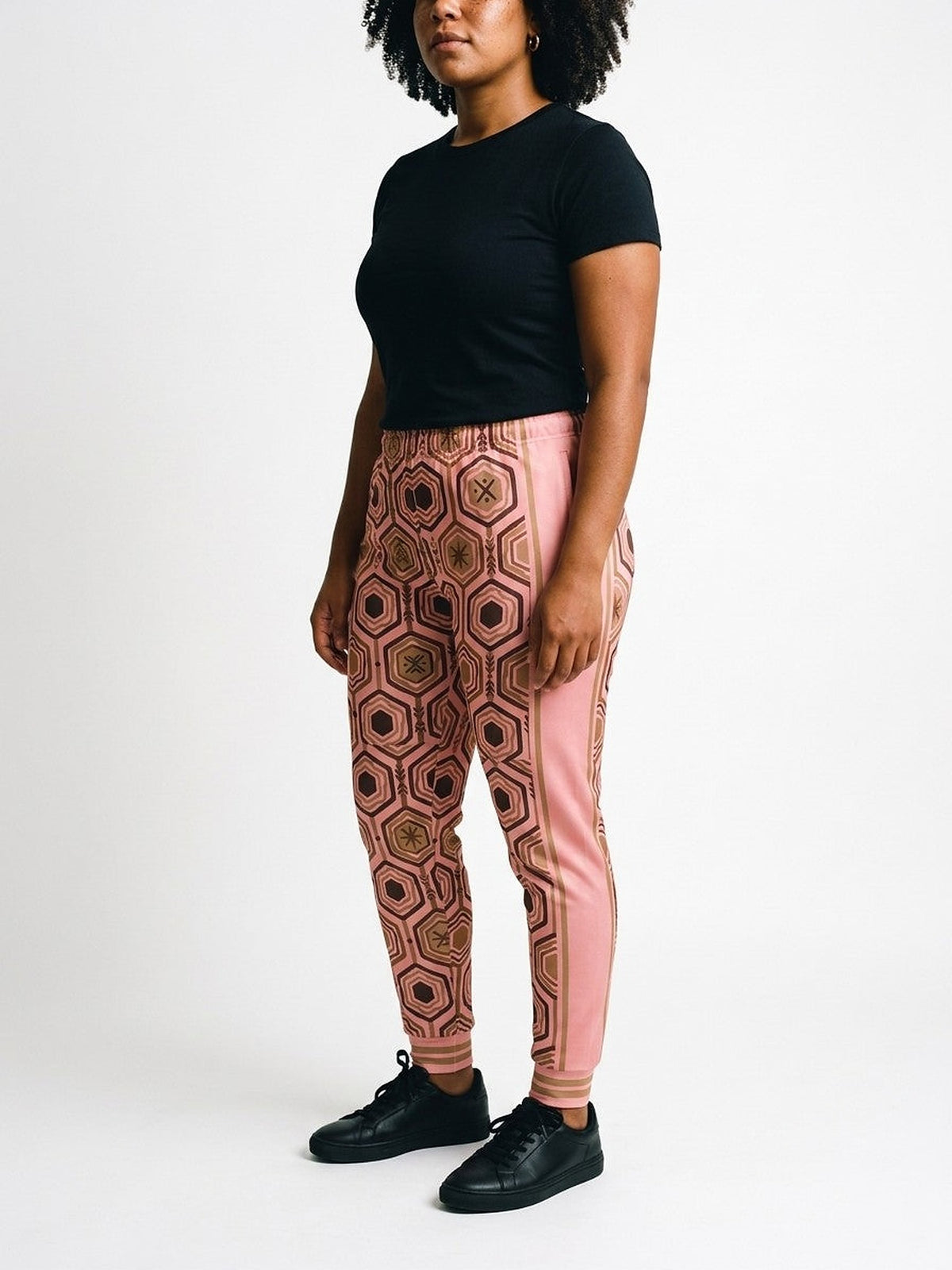 Three-quarter view of AnanseNova™ Women's Joggers in Adaeze Pink on model, pink side panel and bronze side stripes, styled with a black tee
