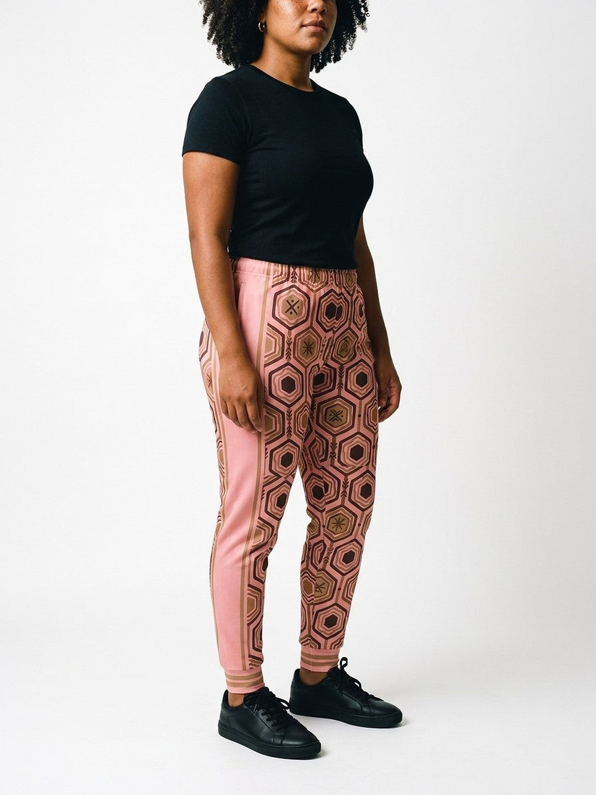 Three-quarter view of AnanseNova™ Women's Joggers in Adaeze Pink on model, pink side panel and bronze stripes, styled with a black tee