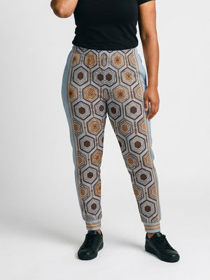 AnanseNova™ Women's Joggers in Igwe Blue, front view on model, full-front bronze and brown hexagon print with light blue side panels, bronze side stripes and striped cuffs | SunBorn