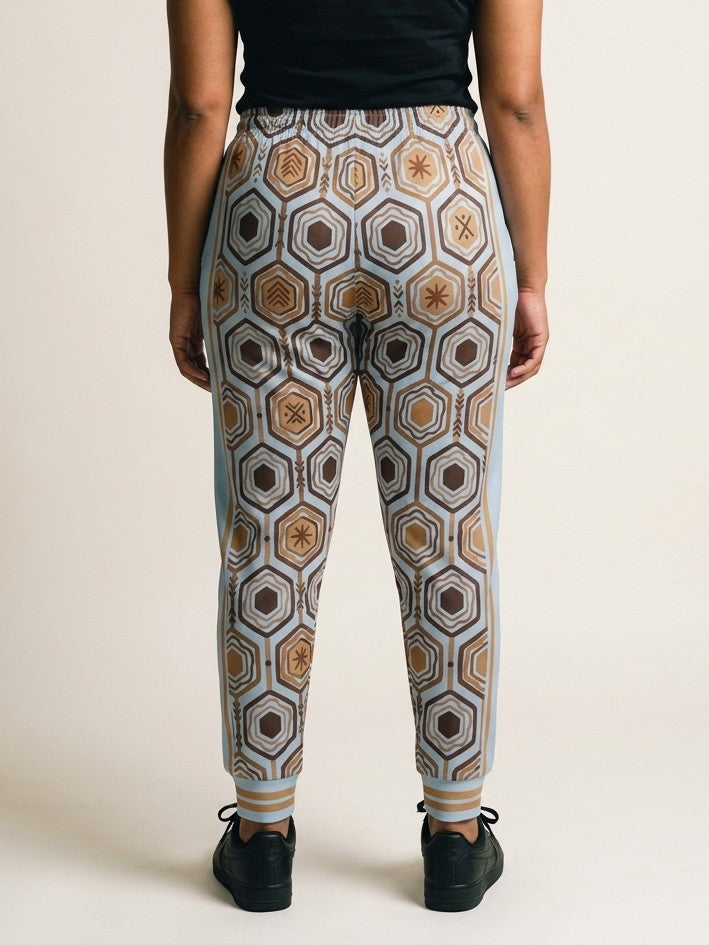 Back view of AnanseNova™ Women's Joggers in Igwe Blue on model, hexagon print continuing across the seat and legs, styled with a black top