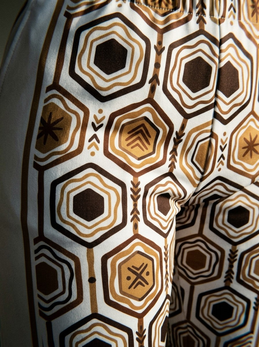 Close-up of the sublimation-printed AnanseNova™ hexagon pattern and seam on Ocha White women's joggers, bronze and deep brown on off-white fleece