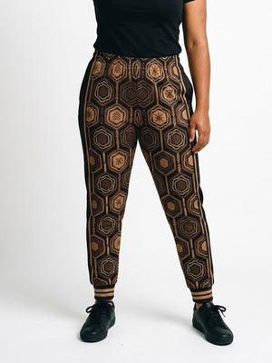 AnanseNova™ Women's Joggers in Oji Black, front view on model, full-front bronze and brown hexagon print with black side panels, bronze side stripes and striped cuffs | SunBorn