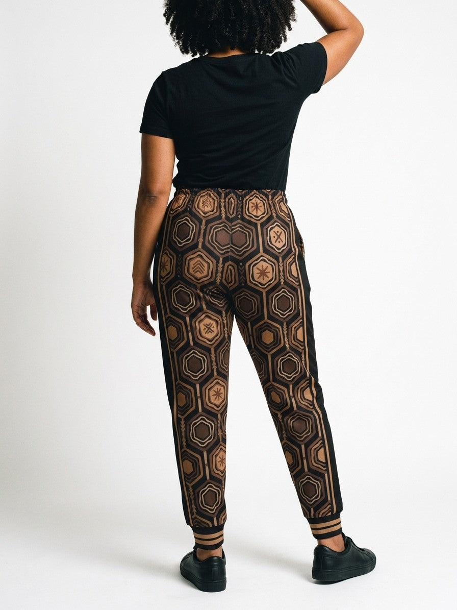 Back view of AnanseNova™ Women's Joggers in Oji Black on model, hexagon print continuing across the seat and legs, styled with a black tee