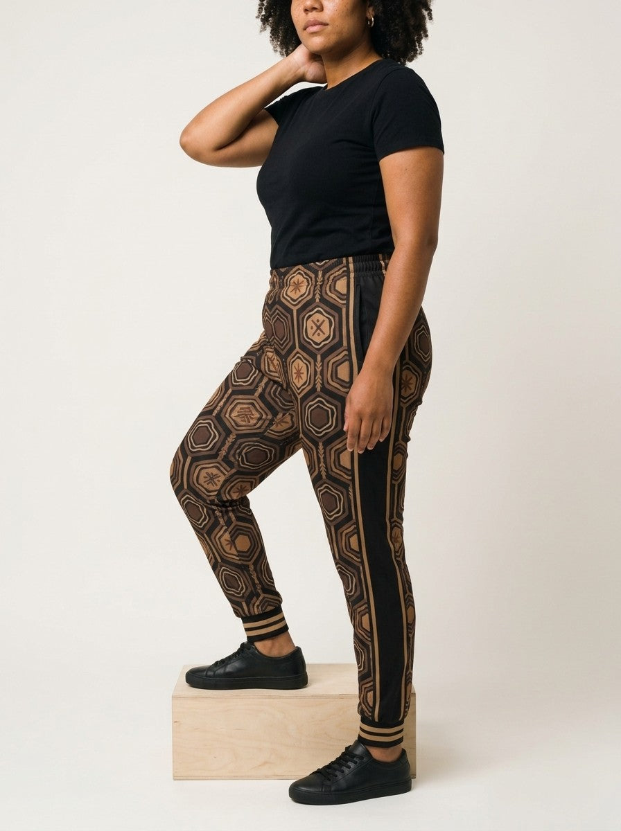 Opposite three-quarter view of AnanseNova™ Women's Joggers in Oji Black on model with one foot on a wooden box, side panel and bronze stripes in profile