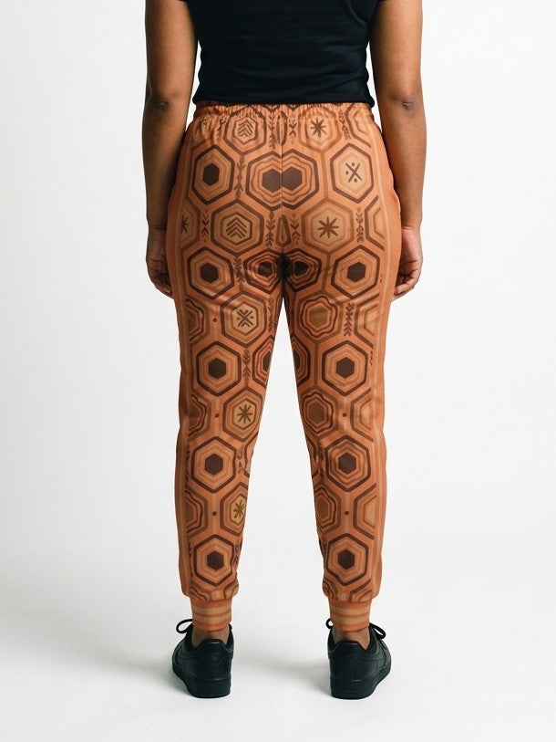 Back view of AnanseNova™ Women's Joggers in Sango Orange on model, hexagon print continuing across the seat and legs, styled with a black tee