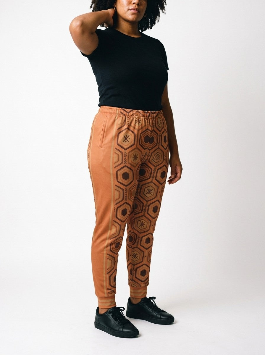 Opposite three-quarter view of AnanseNova™ Women's Joggers in Sango Orange on model, side panel and bronze stripes in profile, styled with a black tee