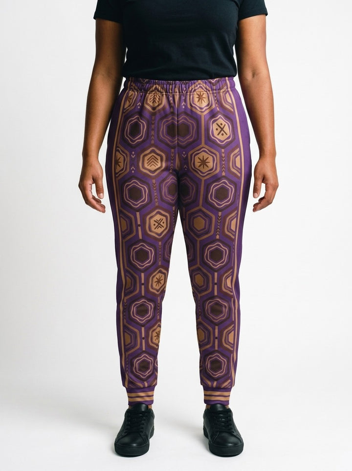 AnanseNova™ Women's Joggers in Ugo Purple, front view on model, full-front bronze and brown hexagon print with purple side panels, bronze side stripes and striped cuffs | SunBorn