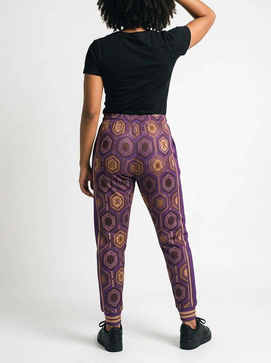 Back view of AnanseNova™ Women's Joggers in Ugo Purple on model, hexagon print continuing across the seat and legs, styled with a black tee