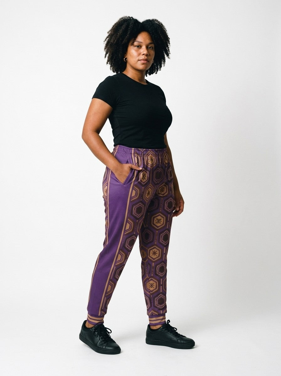 Three-quarter view of AnanseNova™ Women's Joggers in Ugo Purple on model, hand in pocket, purple side panel and bronze stripes, styled with a black tee