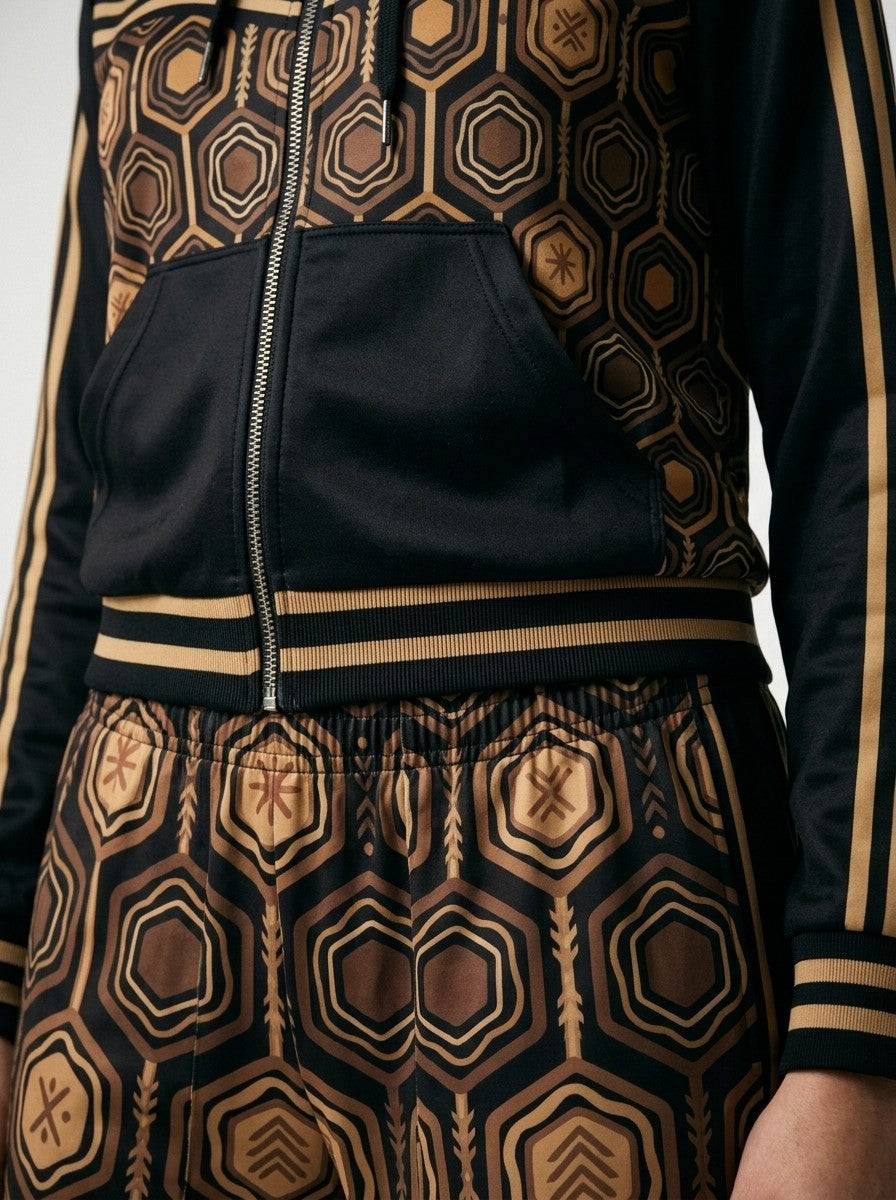 Close-up of the Oji Black AnanseNova™ women's set: zip hoodie pocket, bronze-striped hem and sublimation hexagon print on AkomaDrive™ fleece joggers | SunBorn