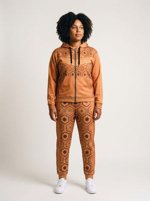 Women's tracksuit set in Sango Orange: AnanseNova™ Zip Hoodie + Joggers on model, front view, bronze hexagon print with chevron chest stripes and full-leg jogger print | SunBorn