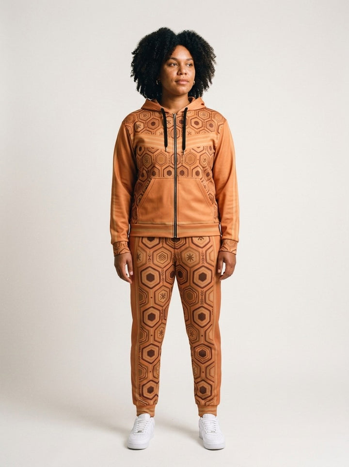 Women's tracksuit set in Sango Orange: AnanseNova™ Zip Hoodie + Joggers on model, front view, bronze hexagon print with chevron chest stripes and full-leg jogger print | SunBorn