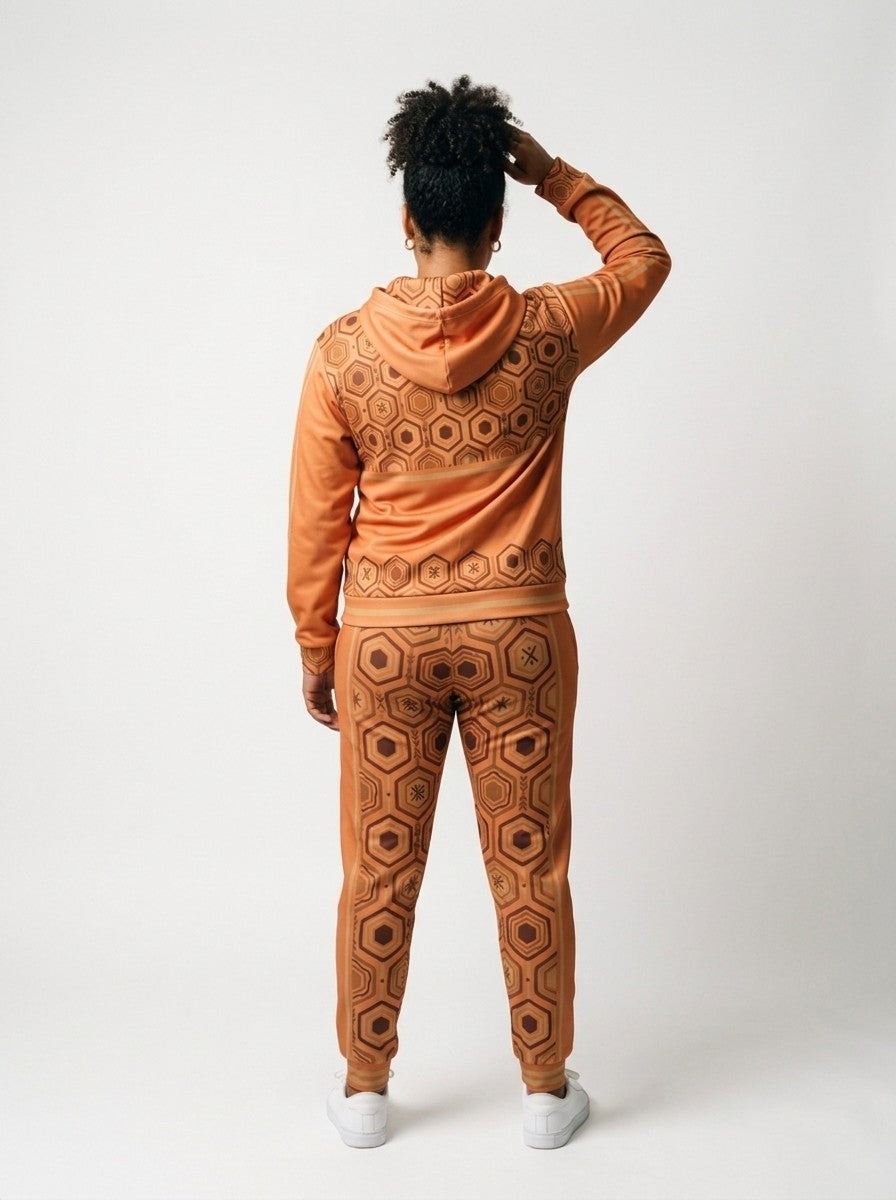 Back view of the AnanseNova™ women's Zip Hoodie + Joggers set in Sango Orange on model, hexagon back yoke, bronze sleeve stripes and printed joggers | SunBorn