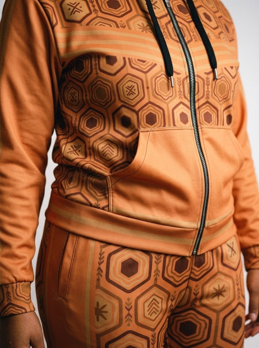 Close-up of the Sango Orange AnanseNova™ women's set: zip hoodie pocket, bronze-striped hem and sublimation hexagon print on AkomaDrive™ fleece joggers | SunBorn