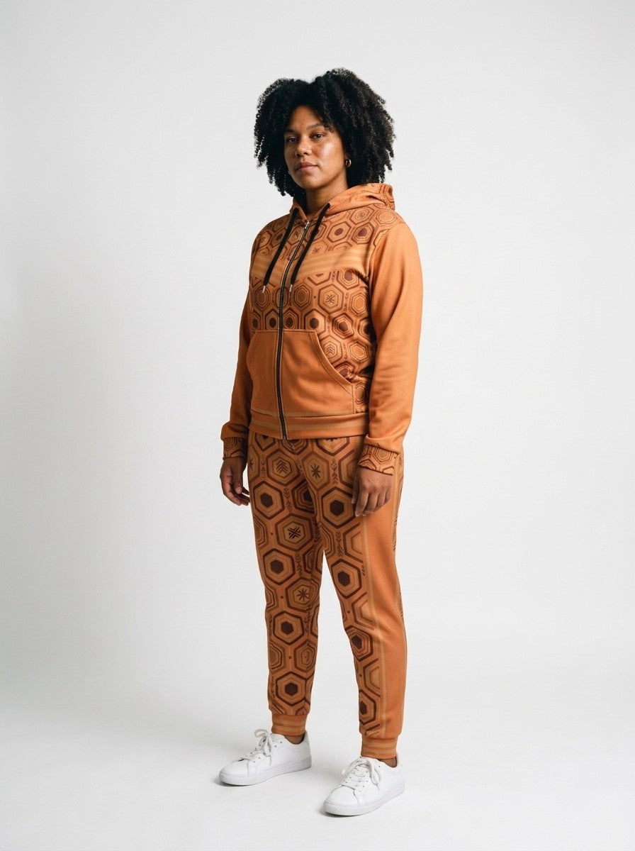Three-quarter left view of the Sango Orange AnanseNova™ women's Zip Hoodie + Joggers set on model, showing the jogger side panel and twin bronze pinstripes | SunBorn