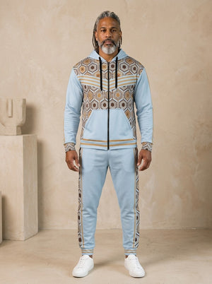 AnanseNova™ Zip Hoodie + Joggers Set in Igwe Blue, front view on model: light blue zip hoodie with brown and gold hexagon print panels and gold sleeve stripes, matching blue joggers with hex side stripes