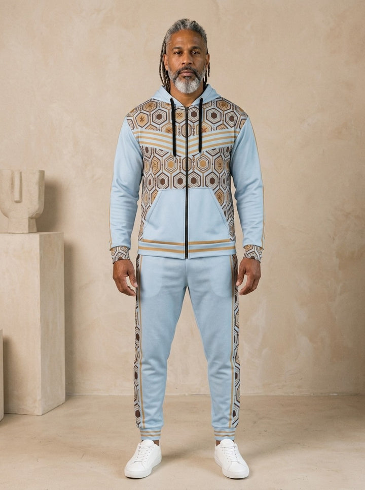 AnanseNova™ Zip Hoodie + Joggers Set in Igwe Blue, front view on model: light blue zip hoodie with brown and gold hexagon print panels and gold sleeve stripes, matching blue joggers with hex side stripes