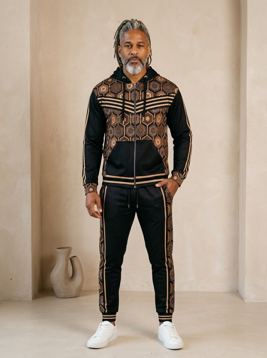 AnanseNova™ Zip Hoodie + Joggers Set in Oji Black, front view on model: black zip hoodie with brown and gold hexagon print panels and gold sleeve stripes, matching black joggers with hex side stripes