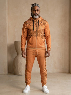 AnanseNova™ Zip Hoodie + Joggers Set in Sango Orange, front view on model: orange zip hoodie with brown and gold hexagon print panels and gold sleeve stripes, matching orange joggers with hex side stripes