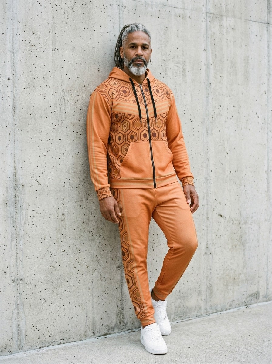 Man leaning against a concrete wall wearing the AnanseNova™ Zip Hoodie + Joggers Set in Sango Orange with white sneakers