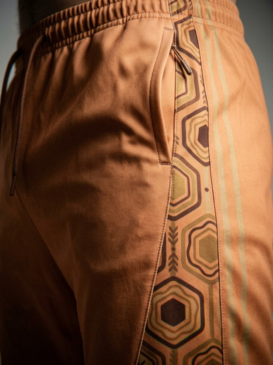 Close-up of the AnanseNova™ Joggers in Sango Orange: side pocket and the brown and gold hexagon side stripe