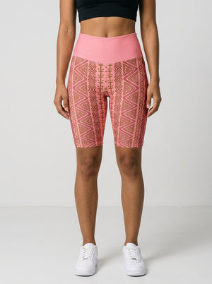 Woman wearing SunBorn N'Donso™ Biker Shorts in Adaeze Pink, front view: high-rise solid pink waistband and Hunter's Road print to mid-thigh