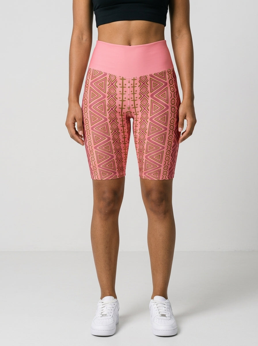 Woman wearing SunBorn N'Donso™ Biker Shorts in Adaeze Pink, front view: high-rise solid pink waistband and Hunter's Road print to mid-thigh