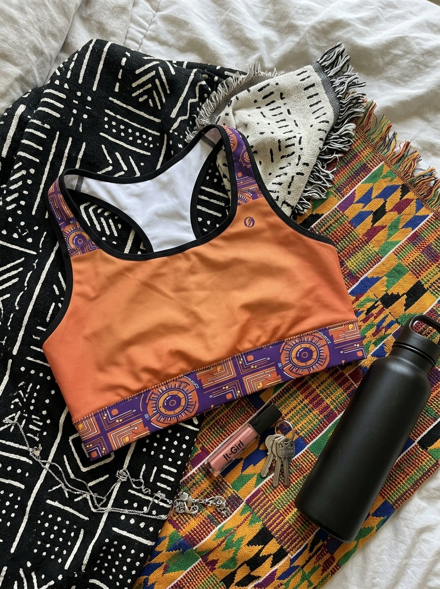 Sankofa Padded Sports Bra in the Sango Orange Kinetic Engine print, flat lay with lifestyle accessories — SunBorn