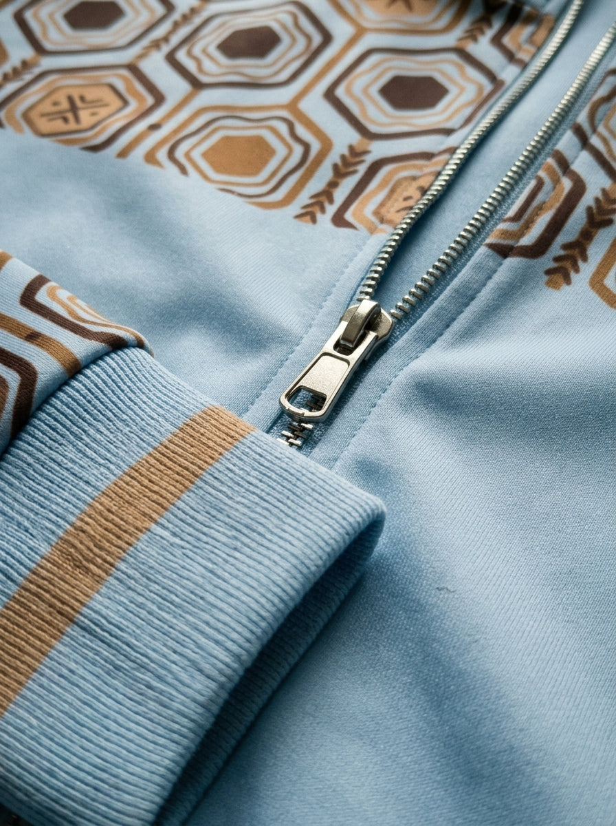 AnanseNova™ Statement Track Jacket in Igwe Blue — close-up of the zipper pull, hexagon print and triple-stripe rib cuff on AkomaDrive™ brushed fleece