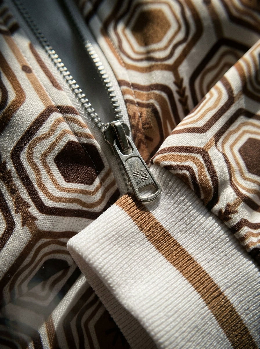 AnanseNova™ Statement Track Jacket in Ocha White — close-up of the zipper pull, hexagon print and triple-stripe rib cuff on AkomaDrive™ brushed fleece