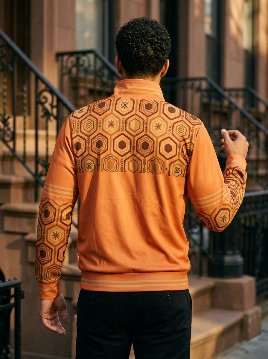 AnanseNova™ Statement Track Jacket in Sango Orange — back view on model on a city street, hexagon print across the upper back and shoulders