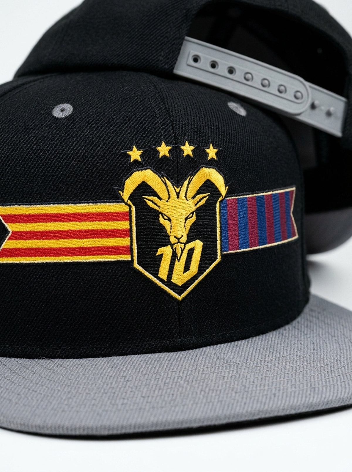 Close-up of the unlimited-colour embroidery on the GOAT Catalan two-tone snapback in Oji Black / Ọnwa Silver — gold goat, No. 10 and the split Senyera and blaugrana banner.